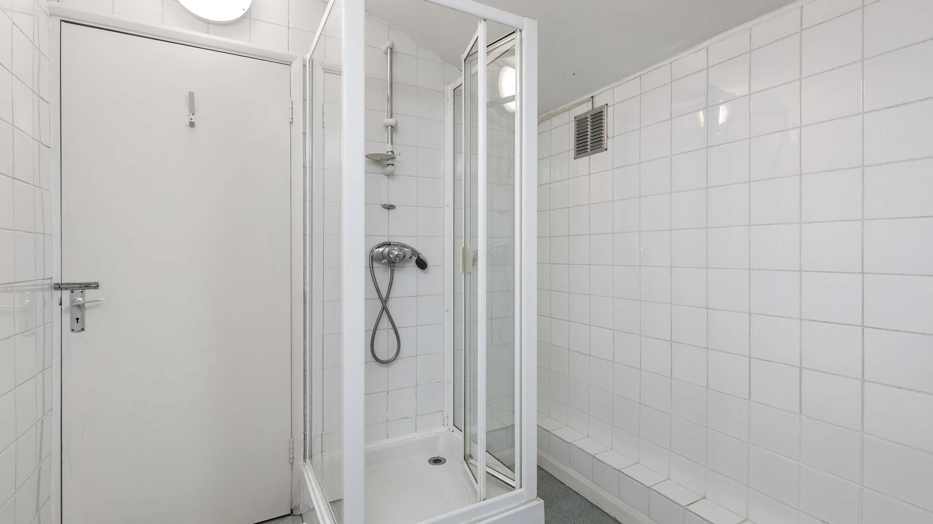 A small, white-tiled bathroom with a corner shower and a closed door.