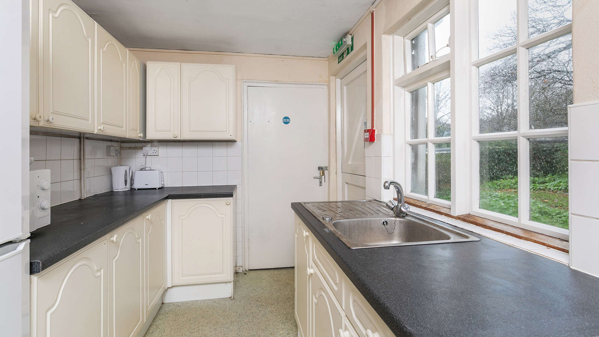 A spacious kitchen with cream-colored cabinets, a black countertop, stainless steel sink, and appliances.