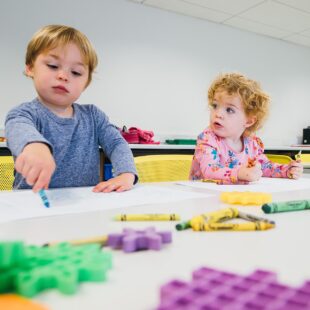 Two children playing with crayons at a table