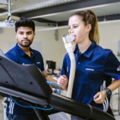 A student running on a treadmill with a breathing mask on, with another student stood reading the data on the screen ahead of them.