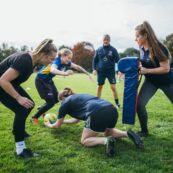 A group of students training their rugby tackling against a tackle bag that one of them is holding.