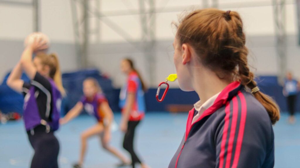 Physical Education student leading a netball session, blowing on a whistle