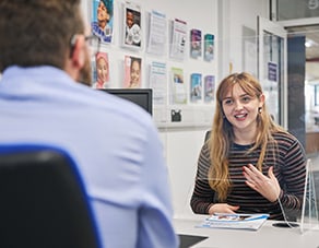 student smiling and talking to member off staff across a table