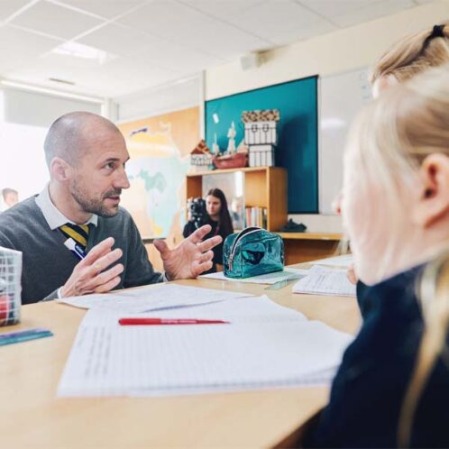 20 Education Secondary Classroom (8) Teacher crouched down to speak to pupils in a classroom