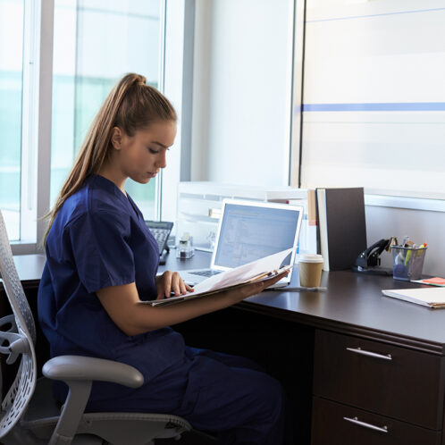 Nurse Wearing Scrubs Working At Desk In Office student in hospital uniform at desk looking over notes