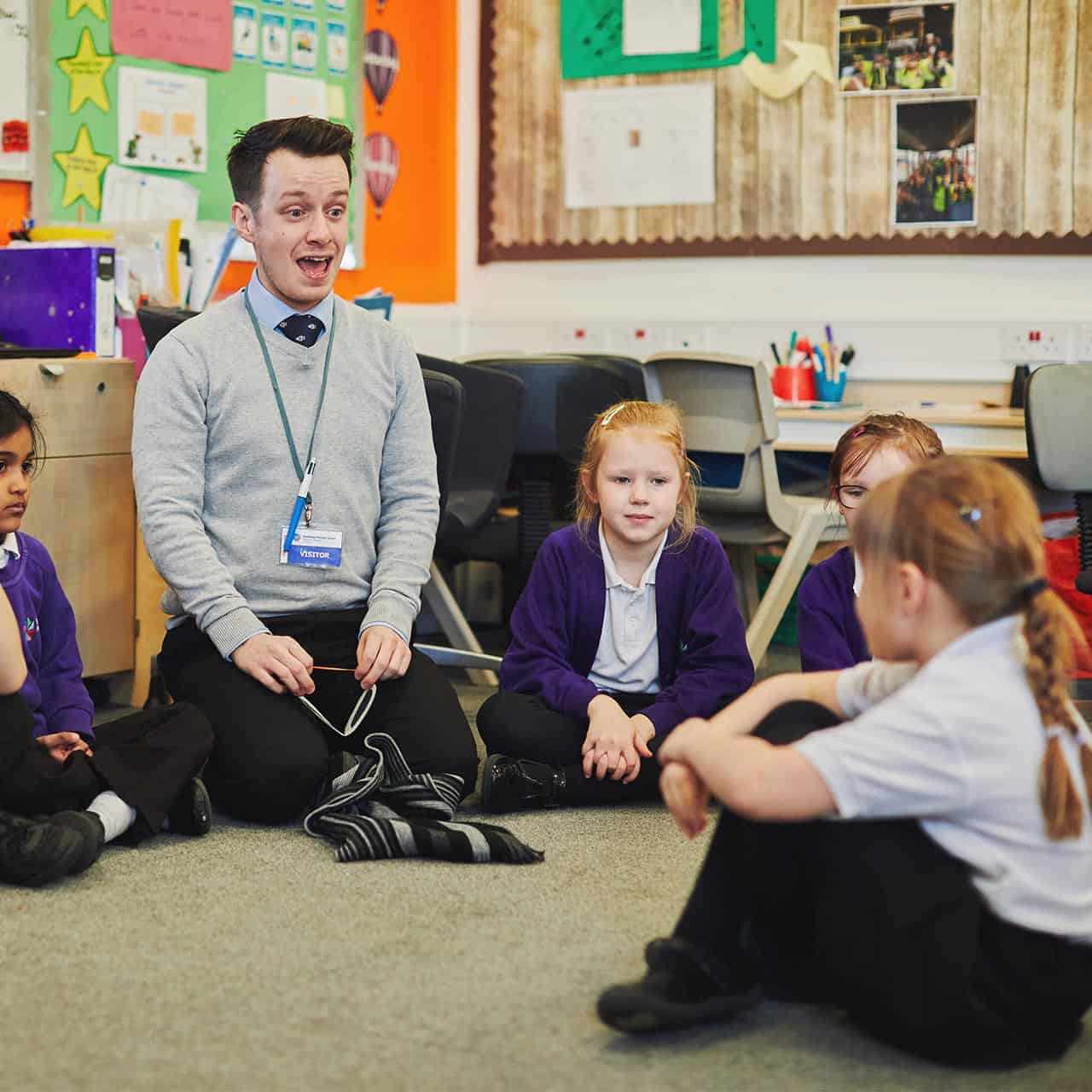 teacher sitting on the floor with primary school class