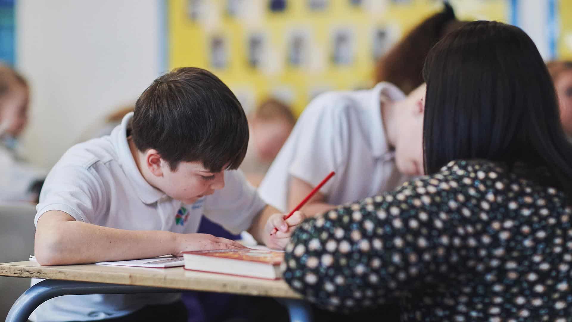 A teaching student crouched over a desk to talk to a pupil