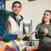 20 Event Management Business 1280x128029 Smiling student wearing high-vis holding a clipboard with another student clapping in the background