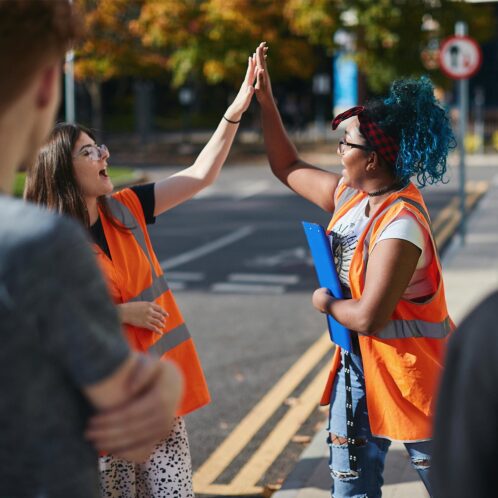 Two students in high-vis high fiving