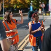 Two students in high vis, one holding a clipboard