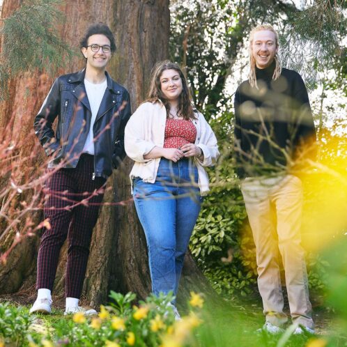 three students standing in front of a tree and smiling