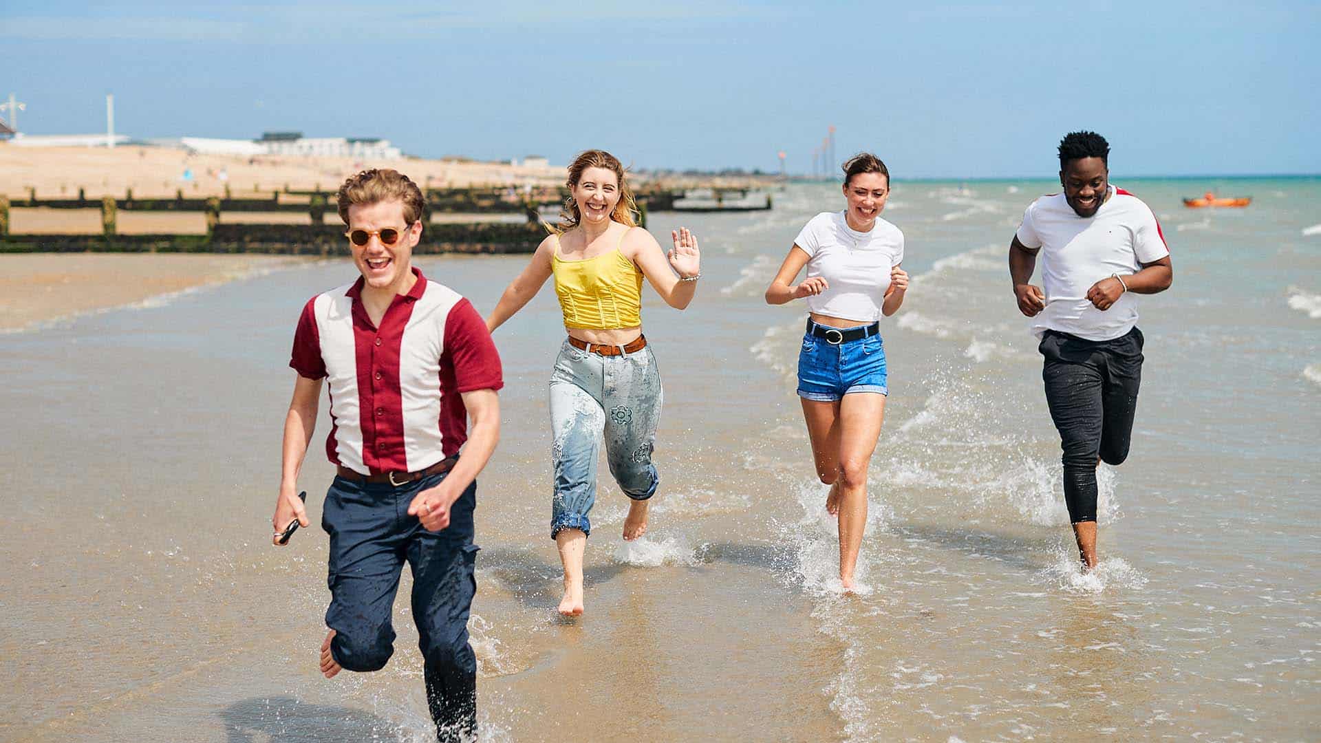 4 students running and laughing on Bognor Regis beach