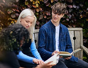 three students sitting on a bench and reading a book