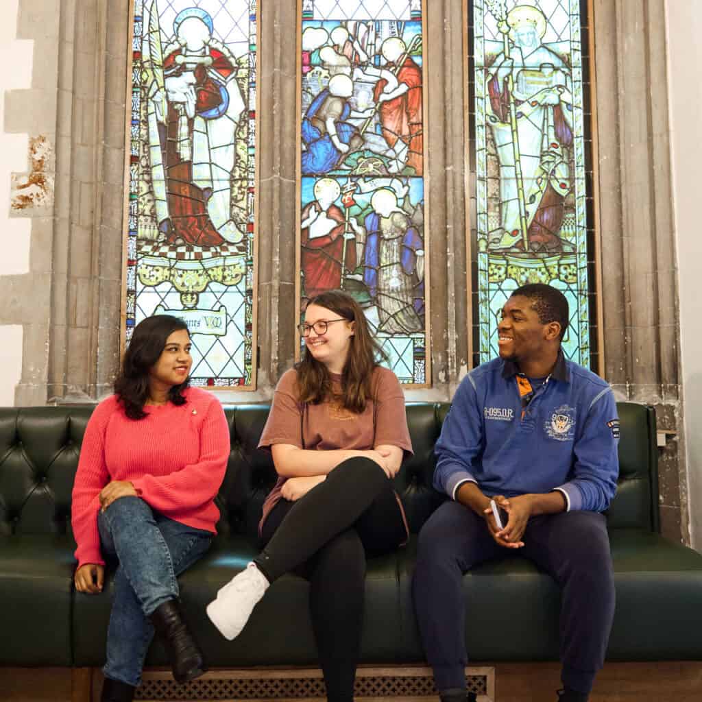 Students sat underneath a stained-glass window in Cloisters