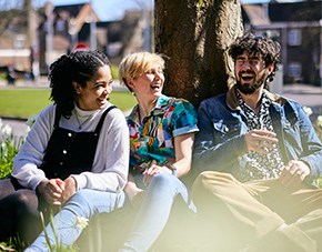 three students leaning against tree laughing