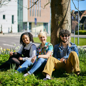 Three students sat on grass next to tree