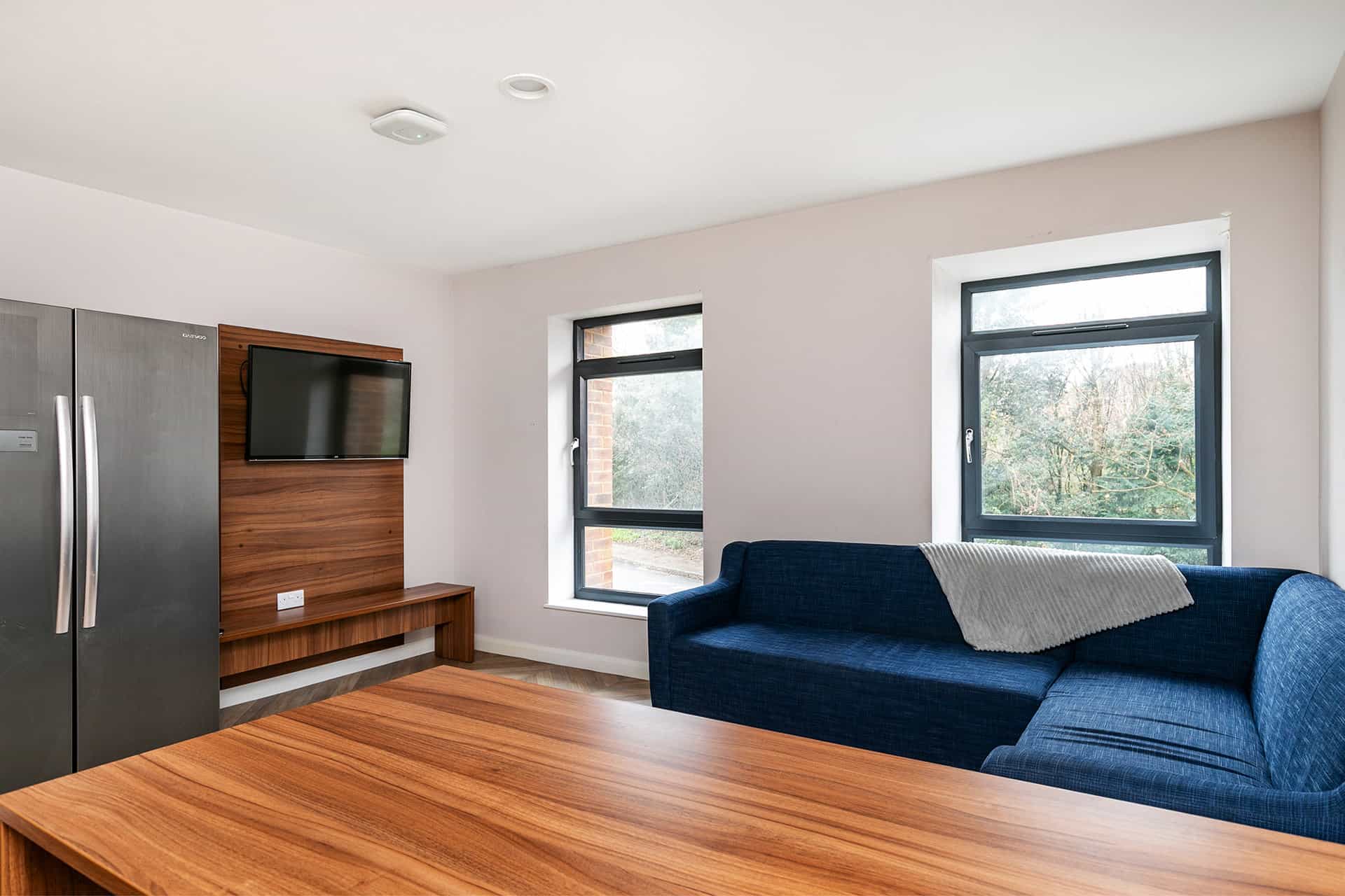 A modern living room with a wooden dining table, sofa with a pillow, mounted TV