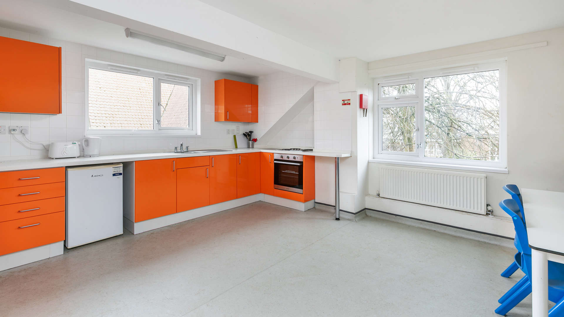 A modern kitchen with bright orange cabinets, white countertops and appliances, and a large window