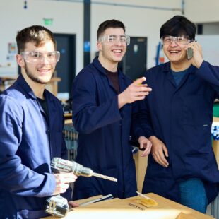 Engineering students together in the workshop smiling with one holding a drill