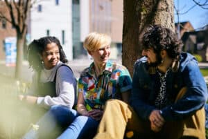 Three students sat next to a tree on campus