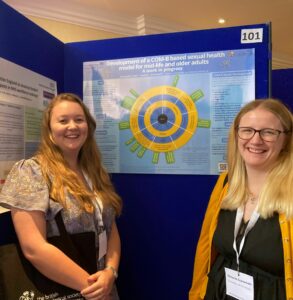 Two research assistants smiling at camera in front of their research poster