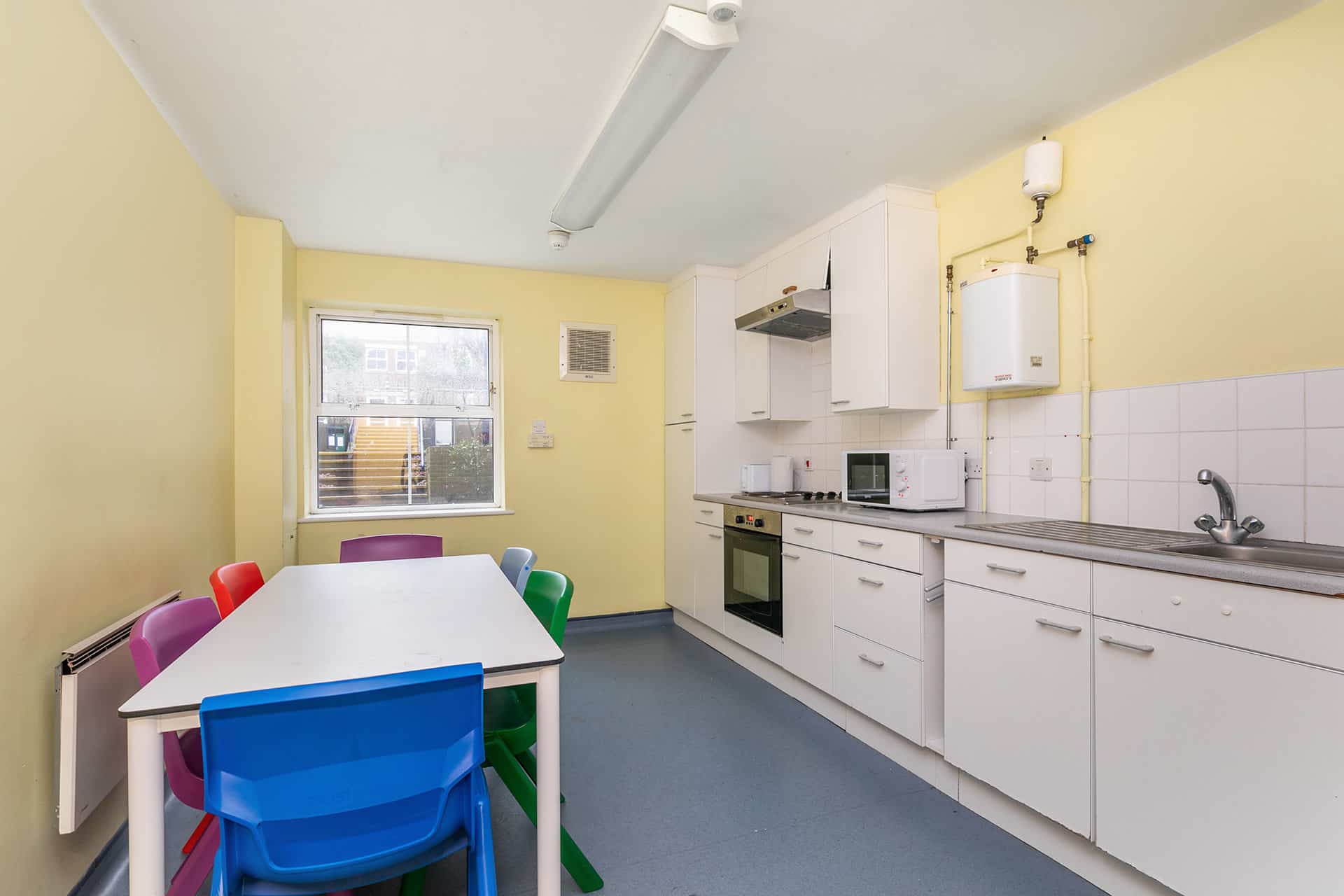 A kitchen with white cabinets and a dining table with colorful chairs.