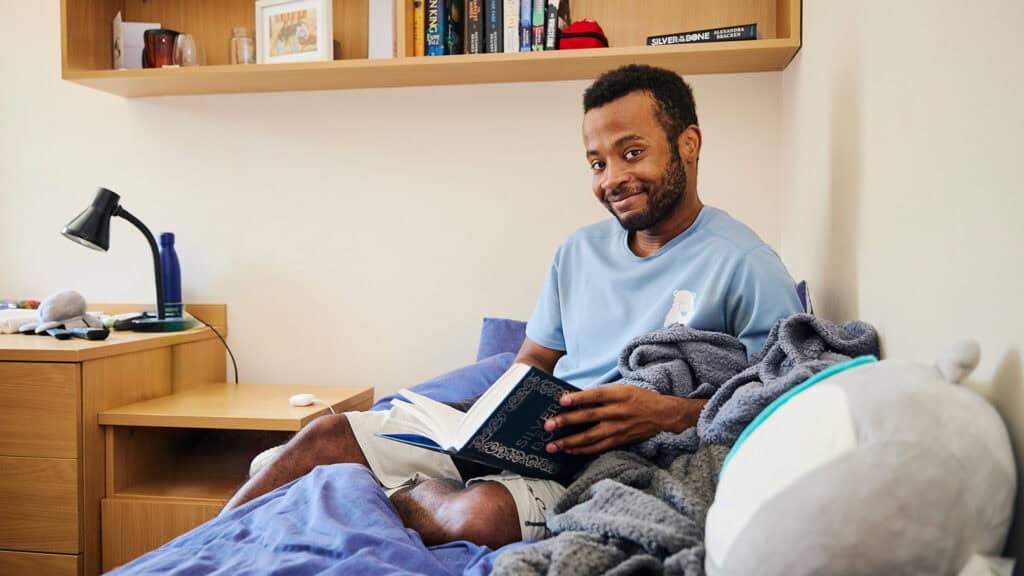 Student sitting on bed reading in dorm room