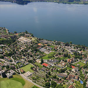 Aerial view of the University of Chichester campus situated by a large lake, showcasing modern buildings, green spaces, and surrounding residential areas in Chichester, West Sussex.