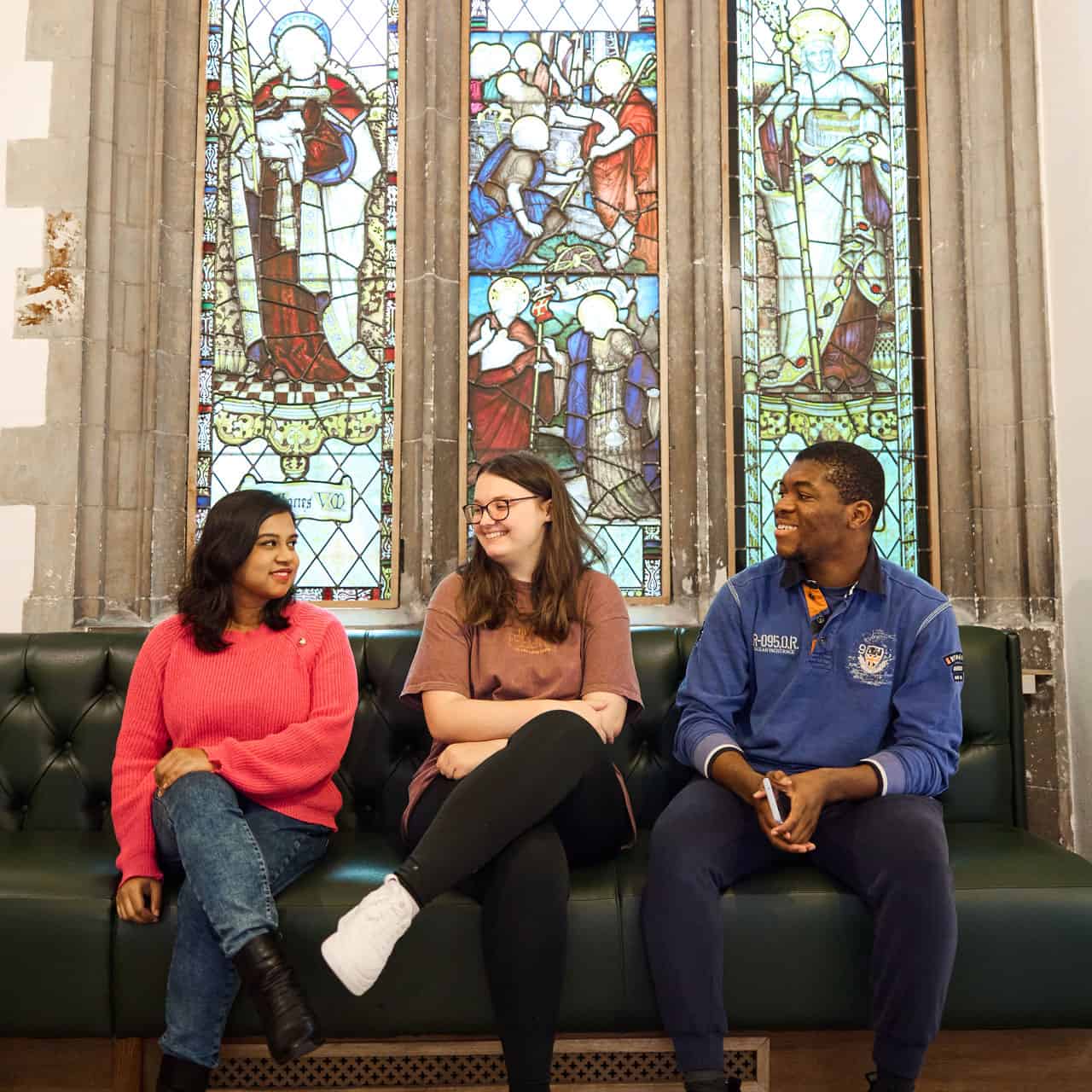 Students sat underneath a stained-glass window in Cloisters