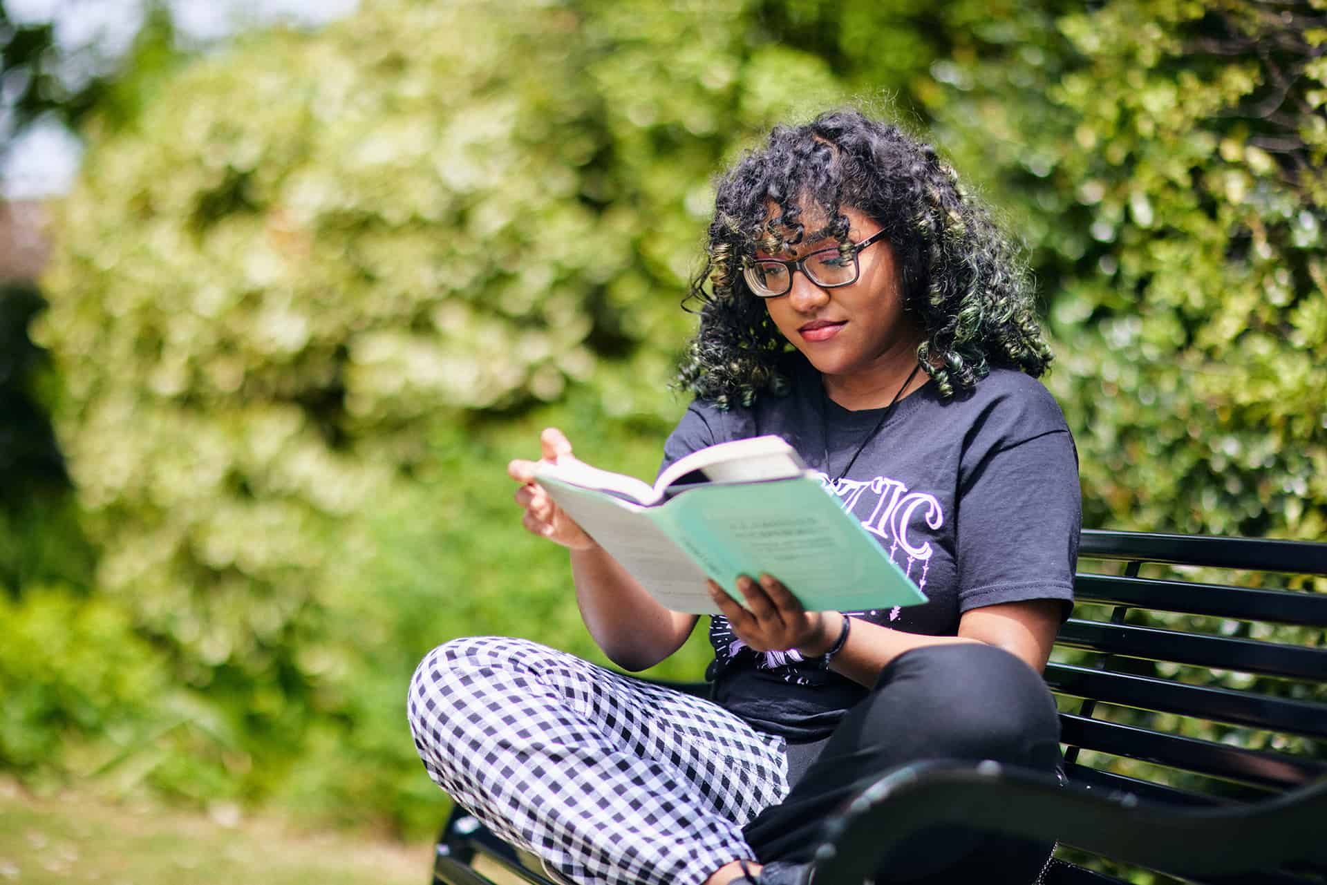 Student sat cross legged on bench reading a book