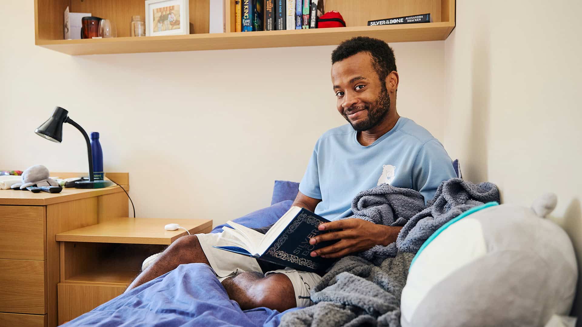 Student sitting on bed reading in dorm room